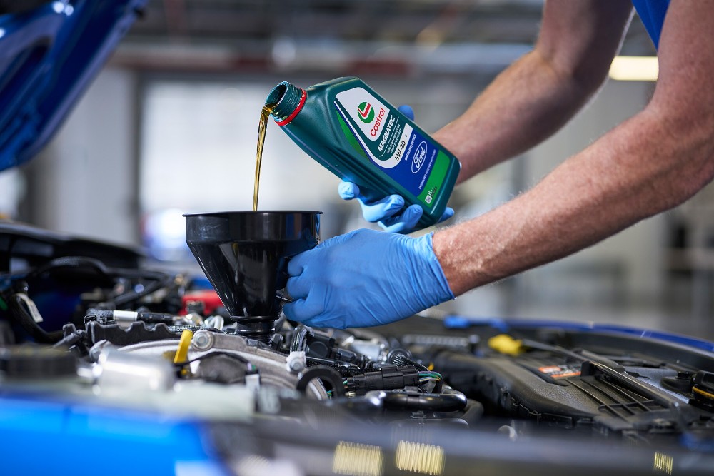 En Ford-tekniker fyller olje på en blå Ford
