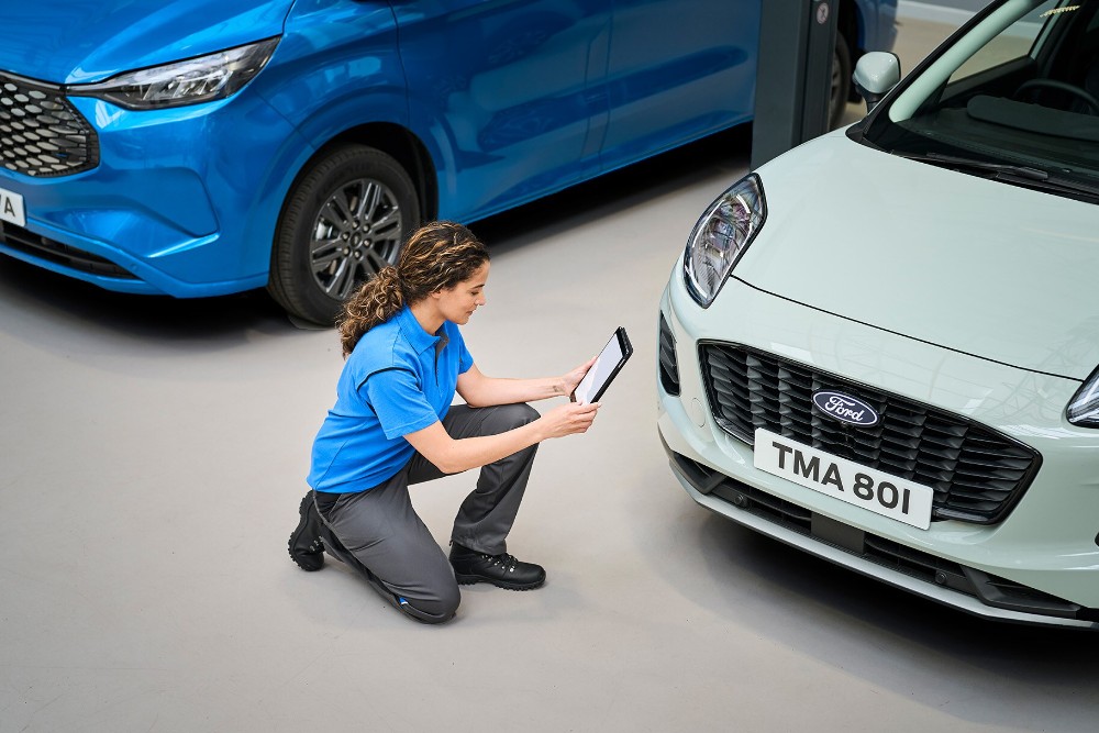 En Ford-tekniker med et nettbrett som utfører EU-kontroll på en Ford Puma med et Ford Pro nyttekjøretøy i bakgrunnen
