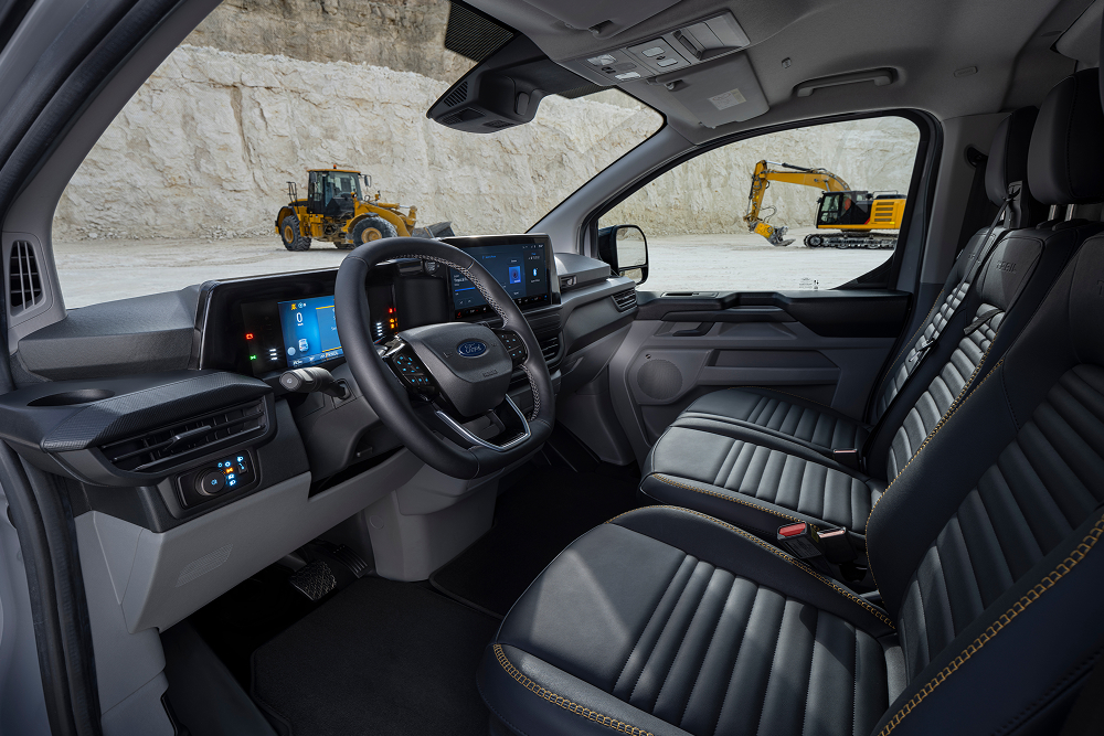  Interiøret i en Ford E-Transit Custom elektrisk varebil, som viser setene og rattet, parkert i et steinbrudd.