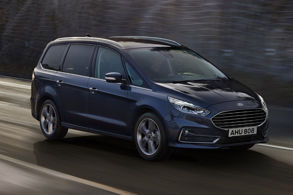 En mørkeblå Ford Galaxy i fart på en vei, sett i front-trekvartsvinkel mot en uklar bakgrunn.