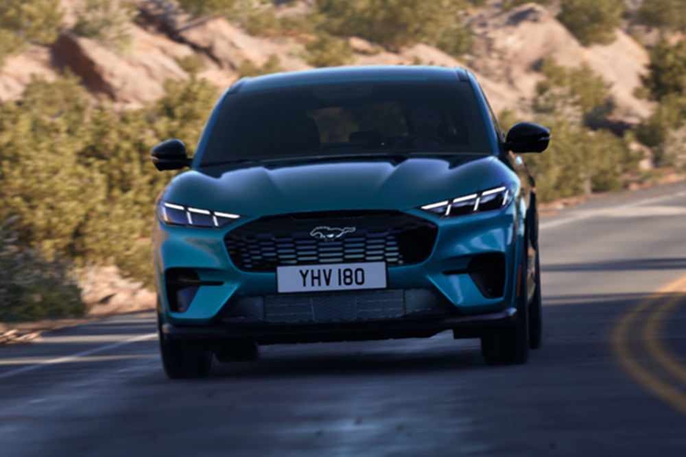 Frontvisning av en blå Ford Mustang Mach-E som kjører på en fjellvei.