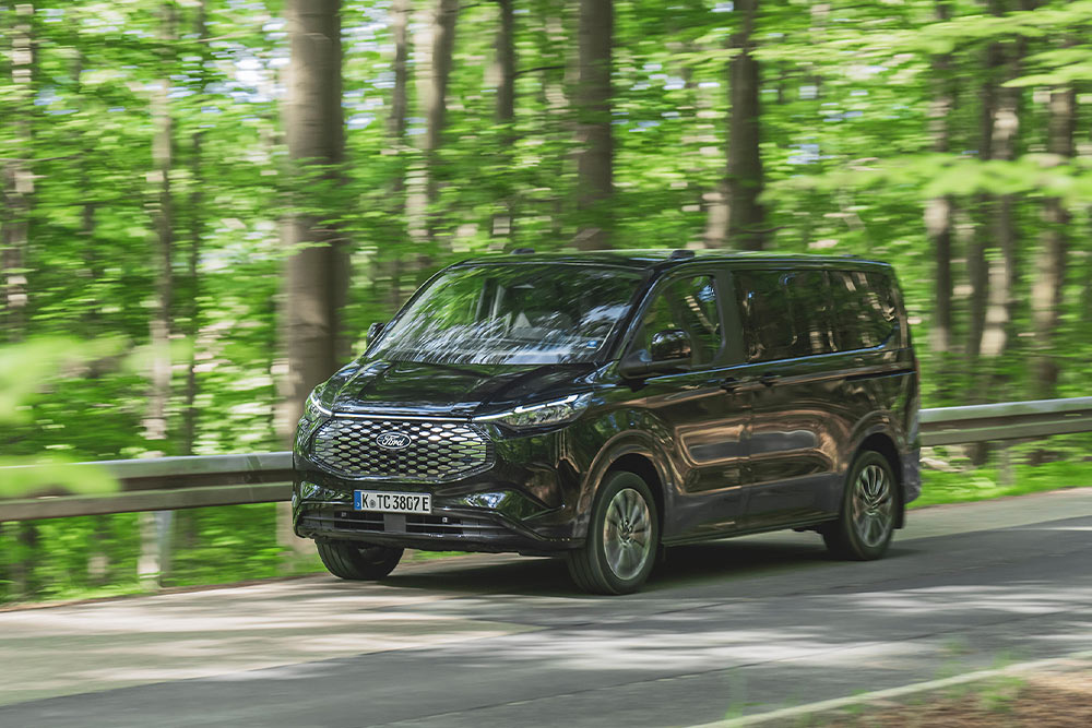 En svart Ford E-Tourneo Custom kjører langs en vei med tre filer.