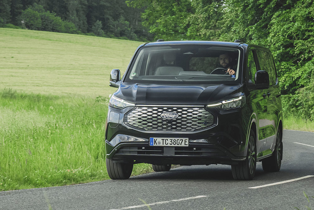 En svart Ford E-Tourneo Custom kjører på en landevei.