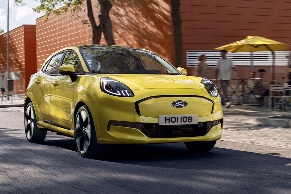 En gul elektrisk Ford Puma® som kjører langs en bygate vist forfra.