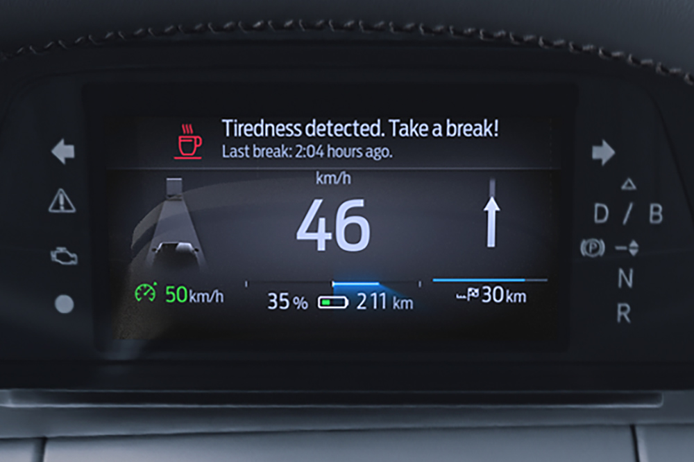 Det digitale kombiinstrumentet i Ford Capri, som viser bilens hastighet og et førervarsel med en advarsel som anbefaler å ta en pause.