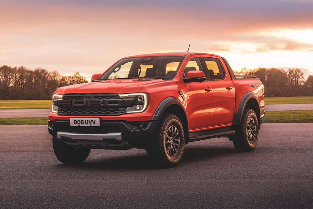 En oransje Ford Ranger Raptor-pickup parkert i et naturskjønt landskap.