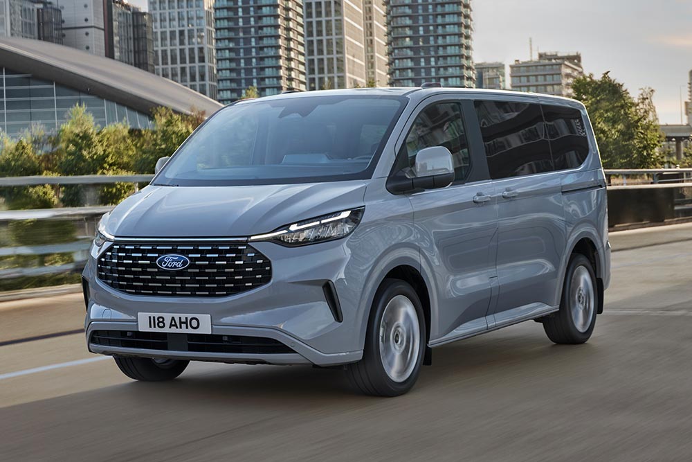 En sølvfarget Ford Tourneo Custom kjører på en byvei.