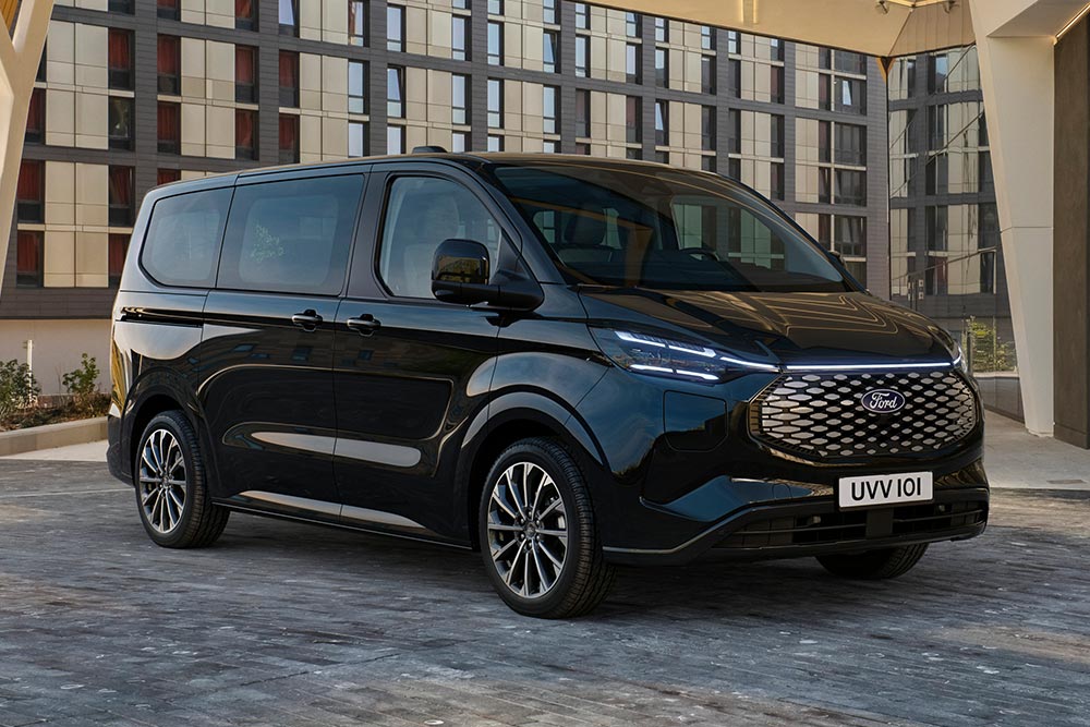 En svart Ford E-Tourneo Custom står parkert foran et moderne bygg.