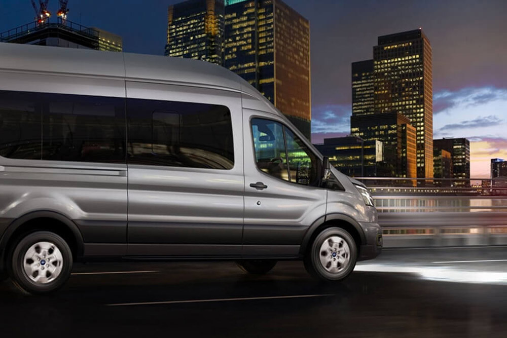 Ford Transit Minibuss som kjører om natten med frontlysene på