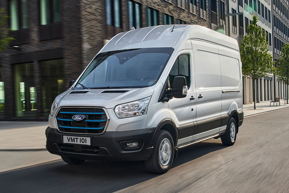 Sølvfarget Ford E-Transit-varebil som kjører på en bygate.