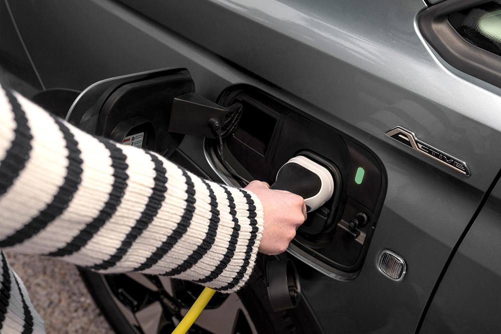 En person som plugger en ladekabel til en ladbar Ford Transit Connect.