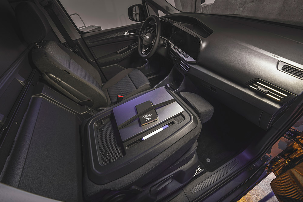 Interiøret i Ford Transit Connect med visning av dashbord, seter, en laptop og en telefon på midtkonsollen.