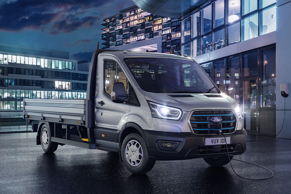 Sølvfarget Ford Transit Chassis Cab parkert foran en moderne bygning om natten.