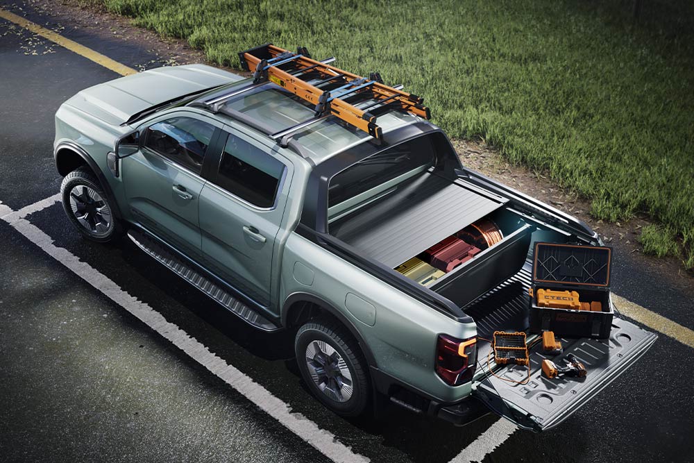 Høyvinkel bakfra av en grå Ford Ranger pickup, lasteplanet åpnet med verktøy og takstativ på en asfaltert overflate.