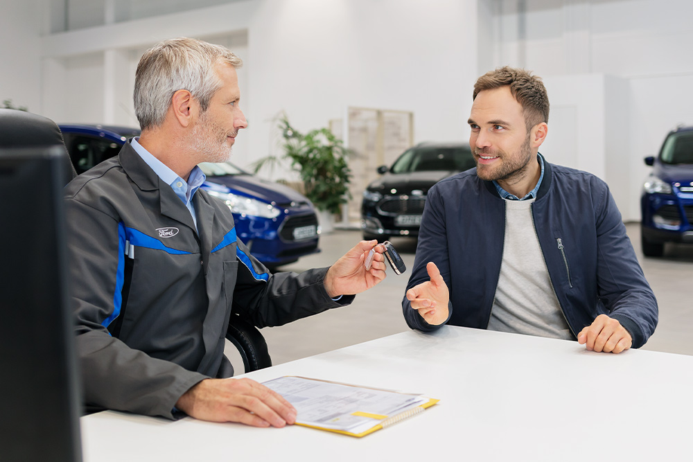 To menn sitter overfor hverandre hos en Ford-forhandler.