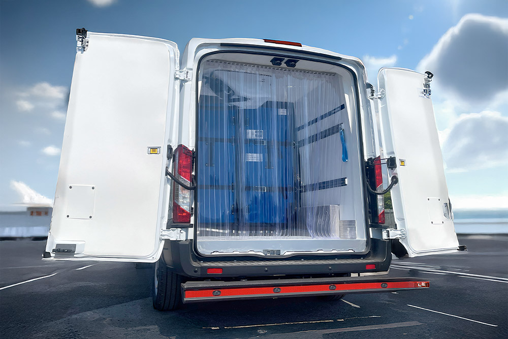 Bakfra-visning av en hvit Ford Transit kjølebil med åpne dører og plaststripegardiner.