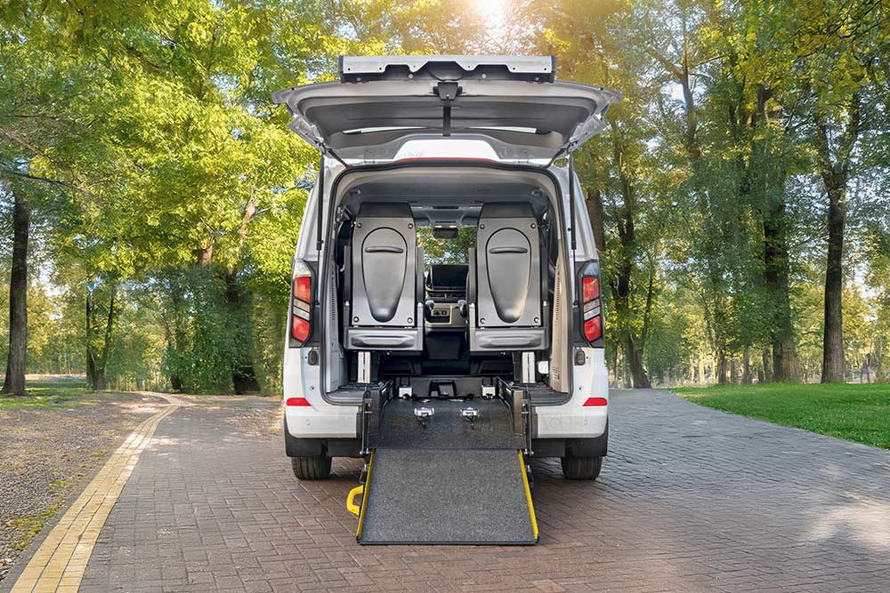 Bakfra-visning av en hvit Ford Transit Custom med åpen bakluke og utplassert rullestolrampe.