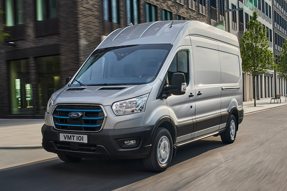 En sølvfarget Ford Transit kjører gjennom et urbant landskap.