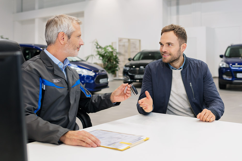 To menn sitter overfor hverandre hos en Ford-forhandler.