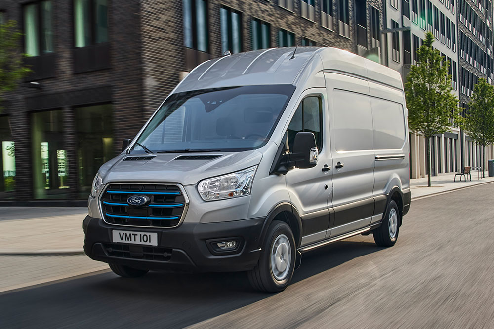 En sølvfarget Ford Transit kjører gjennom et urbant landskap.