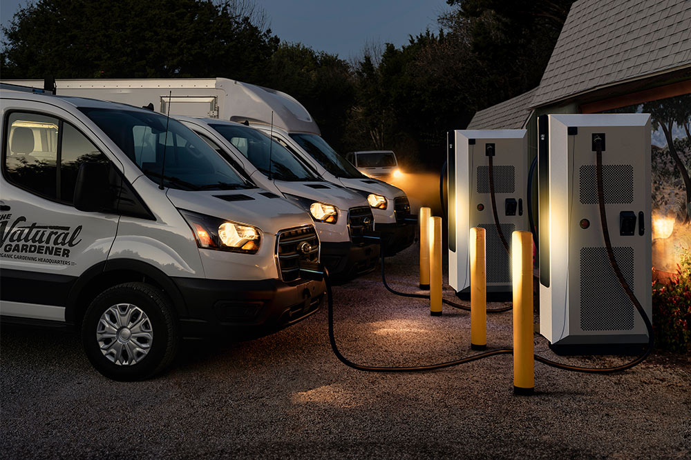 Kveldsscene med Ford elektriske varebiler som lader på en kraftstasjon.
