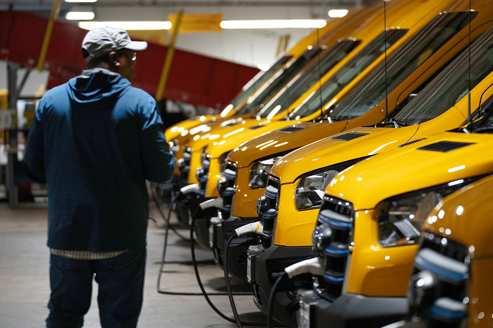En rekke gule Ford elektriske varebiler lades, en mann står ved siden av dem.
