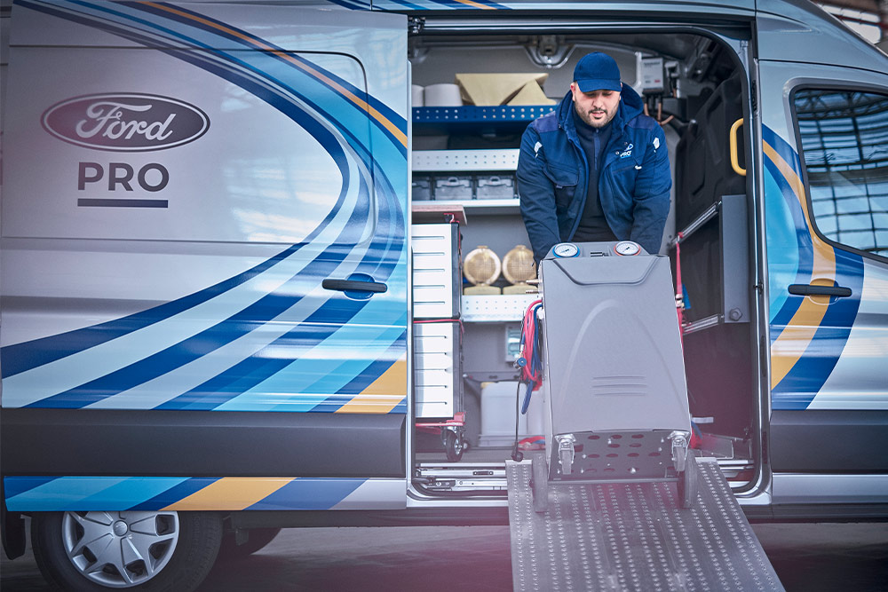 En mobil Ford Pro-tekniker trekker verktøy ut av en Transit varebil foran en bedrift.
