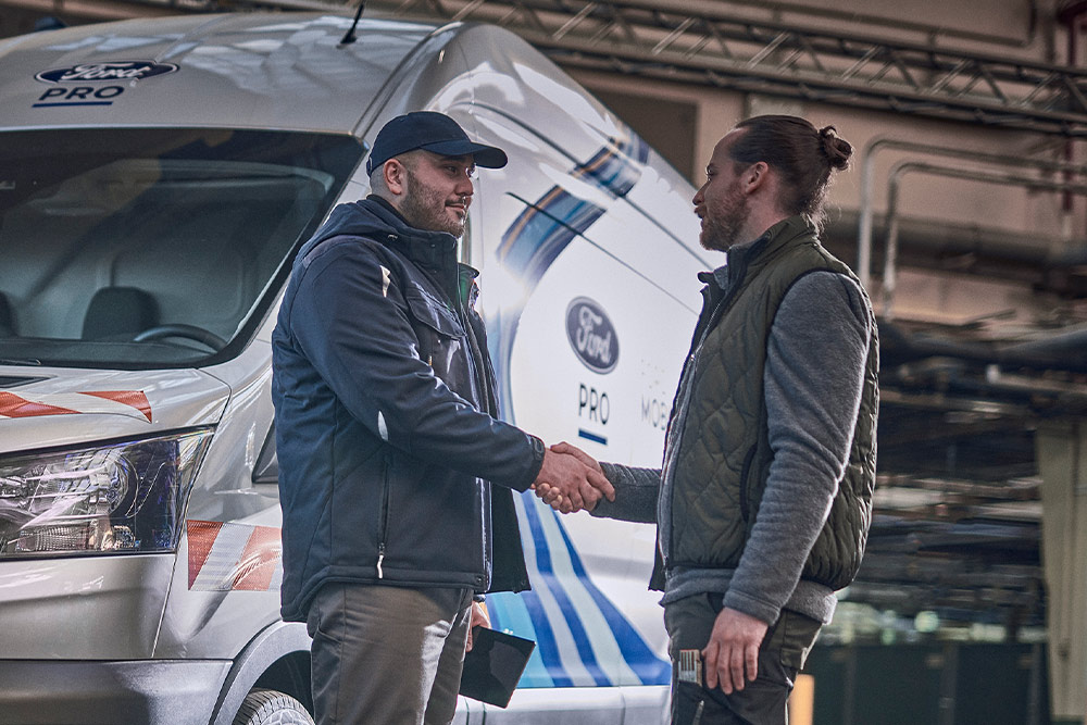 Ford Pro-tekniker snakker med kunde, en Ford Pro Mobile Service varebil er synlig i bakgrunnen.