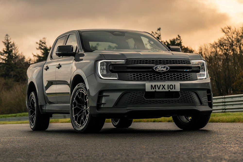 Grå Ford Pro Ranger Plug-in Hybrid parkert på en våt vei, trær i bakgrunnen.