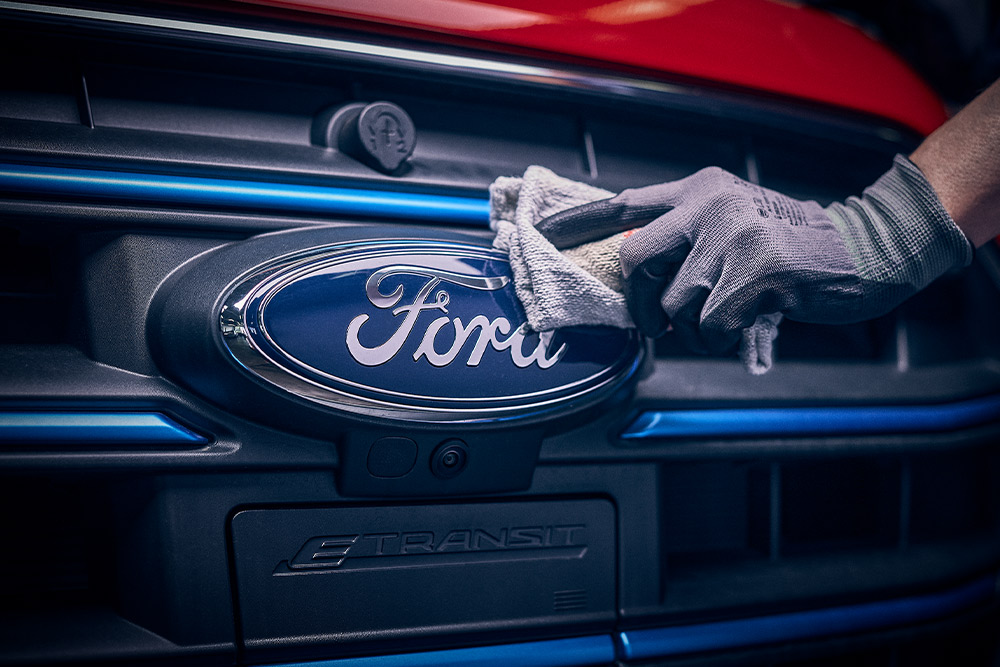 Nærbilde av en tekniker som polerer Ford-logoen foran på en rød varebil.