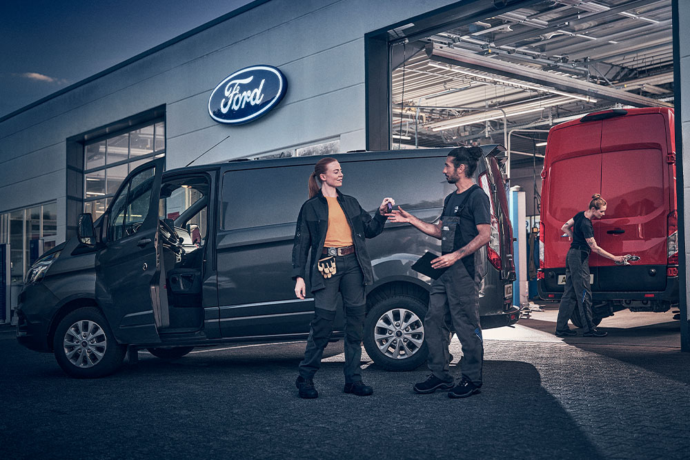 Kunde og Ford-tekniker utveksler nøkler til en varebil foran en Ford-forhandler.