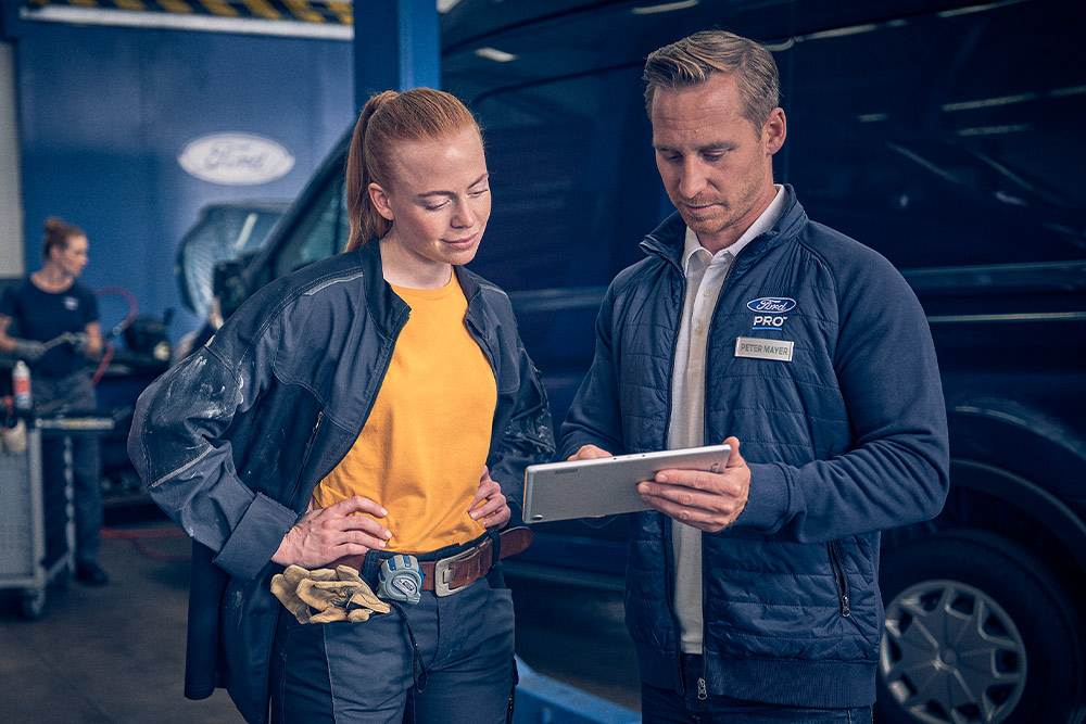 Ford-tekniker og flåtesjef gjennomgår data på et nettbrett i en garasje.